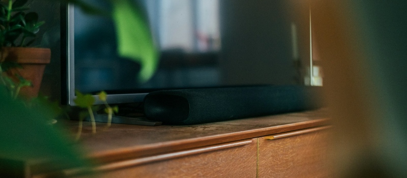 Porta le tue serate cinema a un livello superiore con una soundbar Primo piano di un'elegante soundbar scura su un mobile in legno.