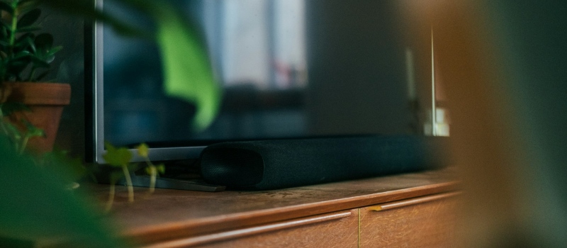Foto ravvicinata di un televisore circondato da piante sopra un mobile TV con una soundbar sotto il televisore.